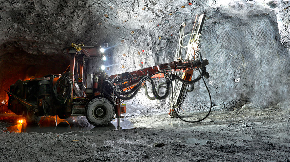 Un jumbo de perforación minera operando dentro de un túnel subterráneo iluminado.