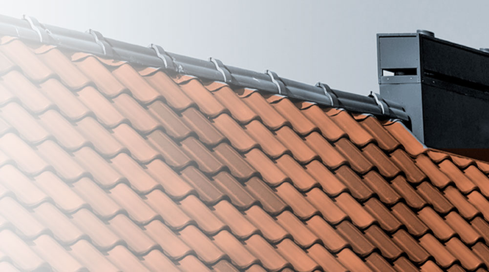 Detail of a sloping roof with Arabic ceramic tiles in tile color and a ventilated metal ridge cap next to a modern chimney